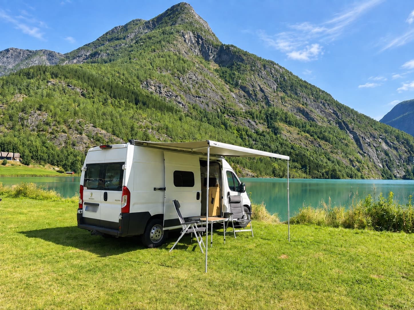 Campervan with the awning extended and camping chairs beside a turquoise mountain lake