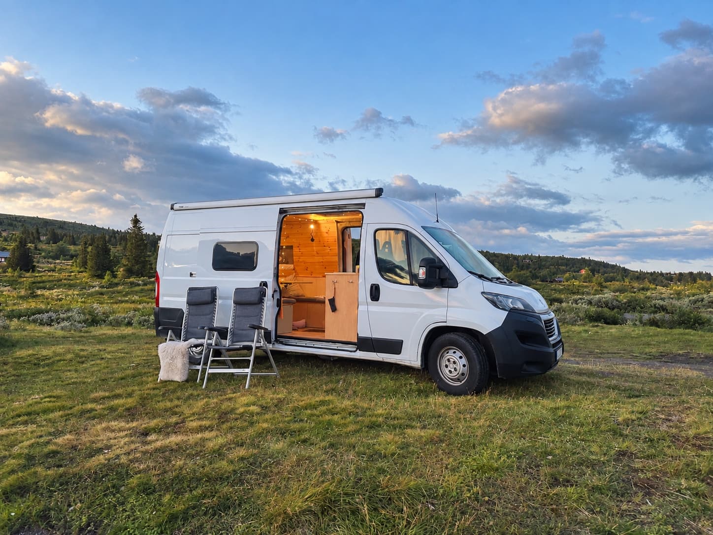 Campervan parked in the mountains at dusk with warm light shining from the open sliding door