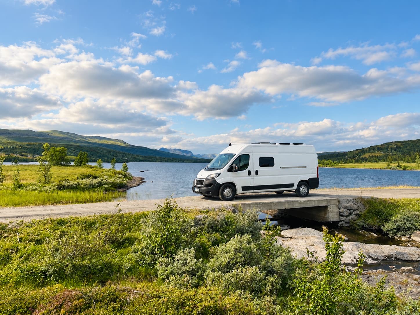 Campervan on a small bridge beside a mountain lake under a blue sky