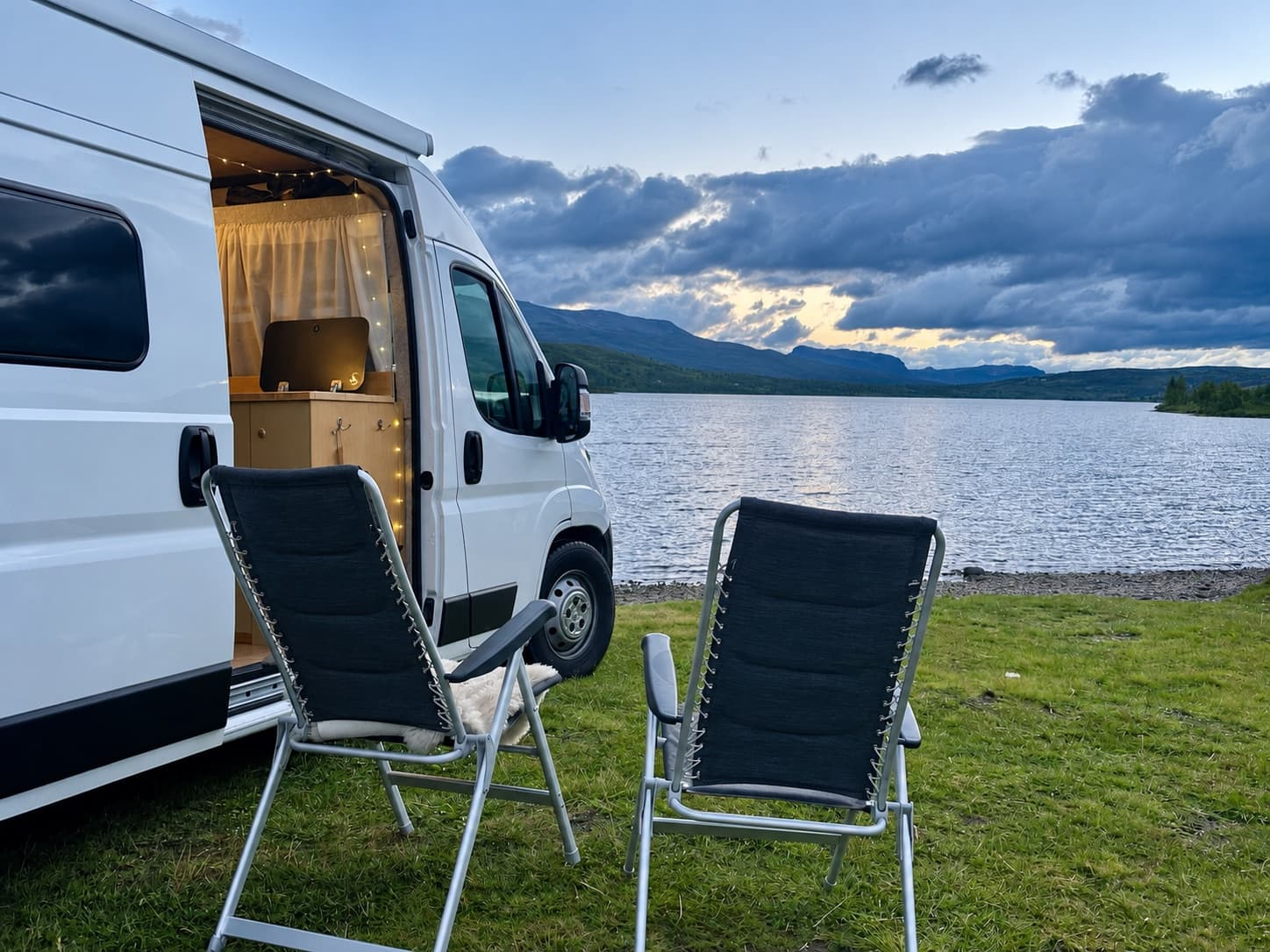 Camping chairs beside the campervan overlooking a mountain lake at dusk