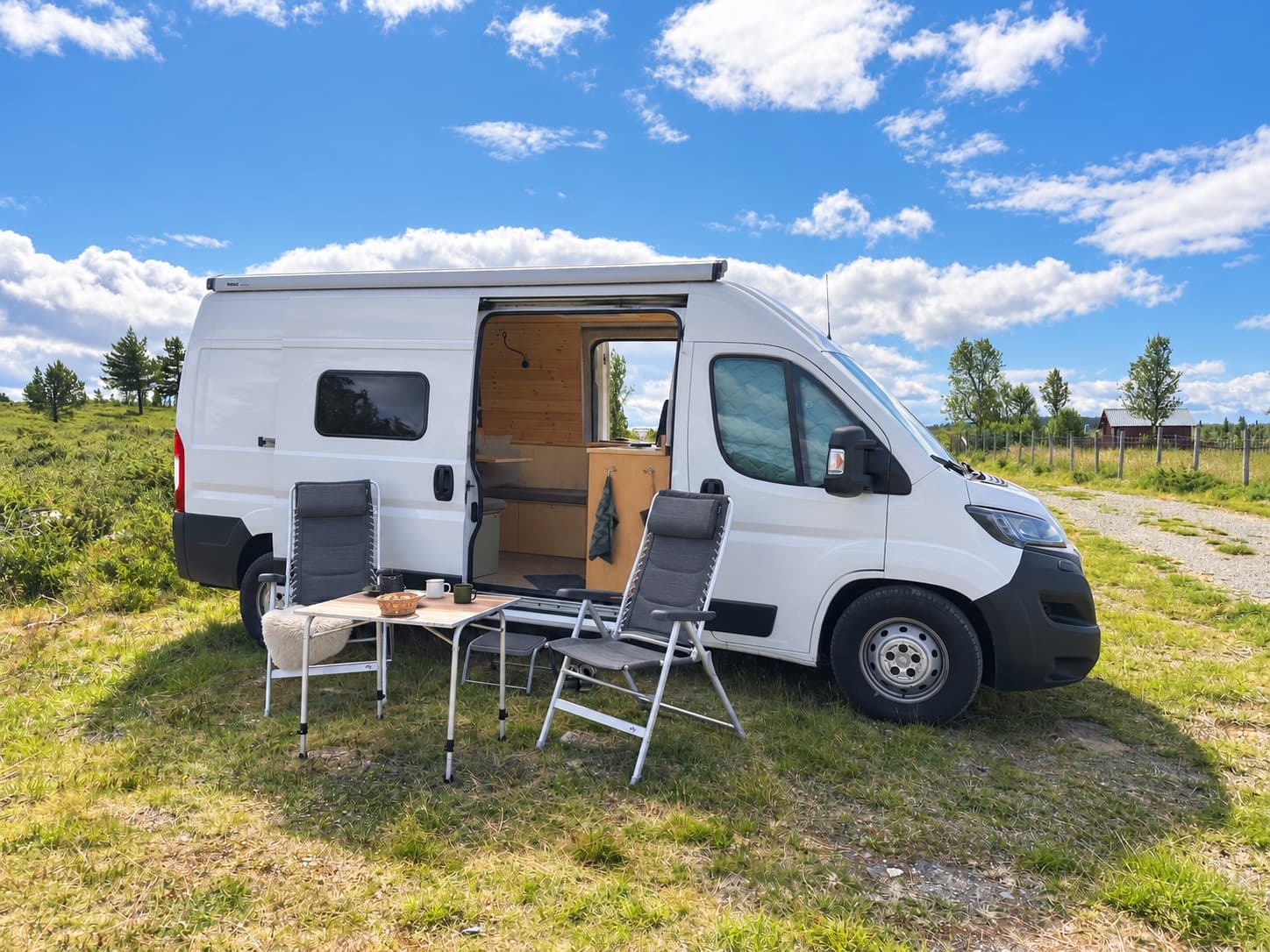 Campervan with an outdoor table and chairs beneath a blue sky